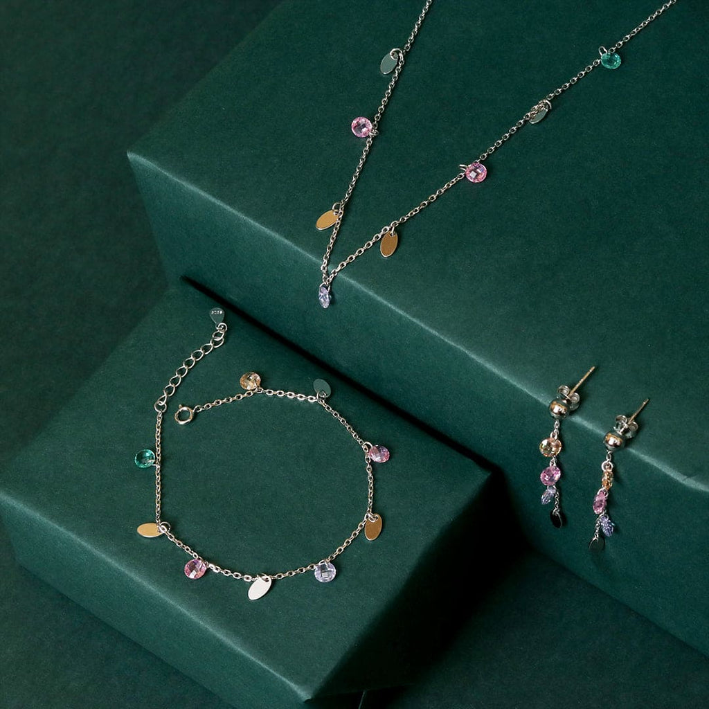 Jewelry set with silver chain necklace, charm bracelet, and pink-teal drop earrings.