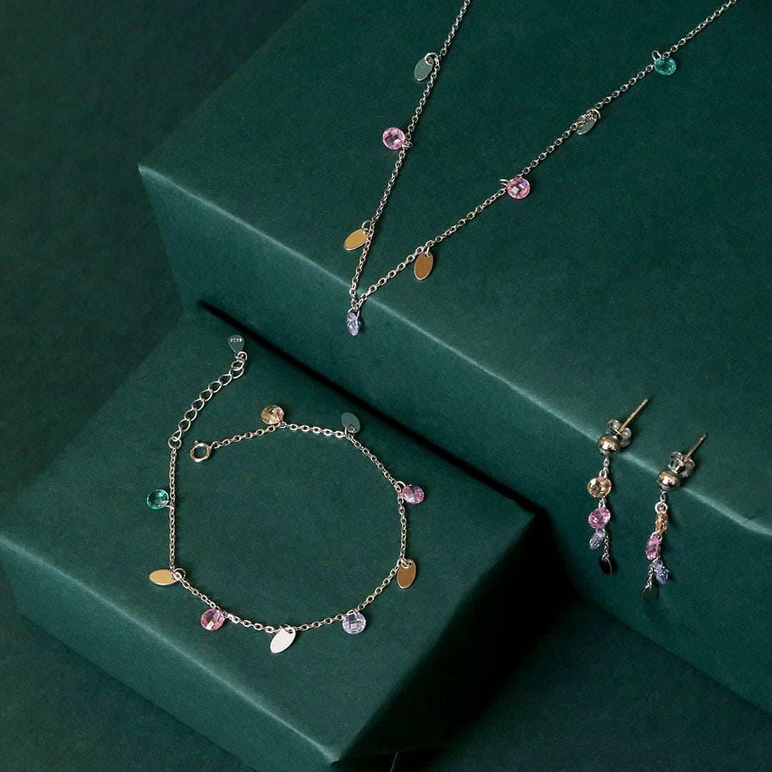 Jewelry set with silver chain necklace, charm bracelet, and pink-teal drop earrings.
